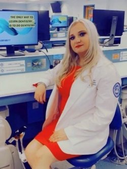 Amela Music profile picture in white coat in the dental lab.