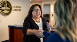 Student Services employee shakes hands with student.