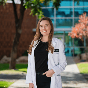 Student posing outside on campus in white coat