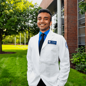 Student posing on campus in white coat