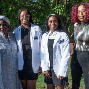 Two students wearing their white coats standing with their families.