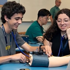 High school students practice using stethoscope on arm simulator.