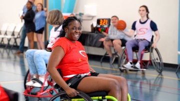 Smiling young woman strapped in a wheelchair. She and others are playing in the wheelchair basketball tournament.
