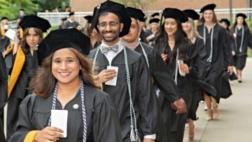 Graduates line up for the processional in black caps and gowns carrying their name cards in their hands.