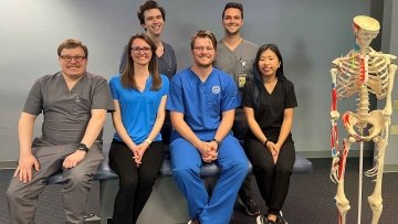 Six AZCOM Scholars sitting on bench near skeleton.