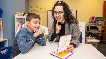 Speech-language pathologist reads out loud with young boy.