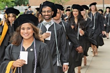 Graduates line up for the processional in black caps and gowns carrying their name cards in their hands.