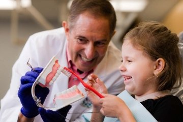 dentist showing child how to brush teeth