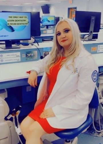 Amela Music profile picture in white coat in the dental lab.