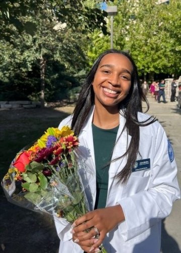 Physical Therapy student Alicia Madden in a white coat holding a bouquet of flowers.