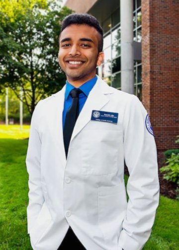 Student posing on campus in white coat