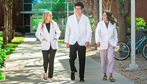 Three students in white coats walking around Glendale campus