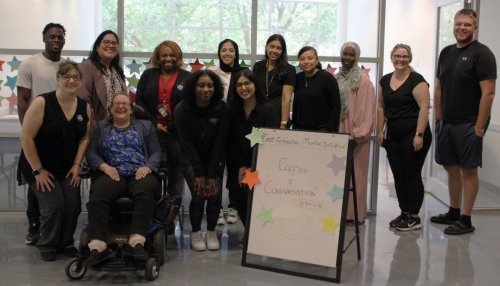 Gathering of students and University staff by the coffee and conversation poster.