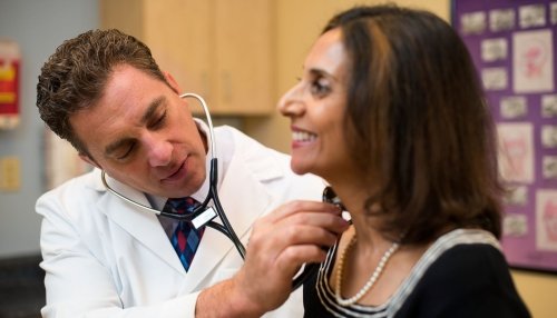 Doctor uses stethoscope to listen to female patient's heartbeat.