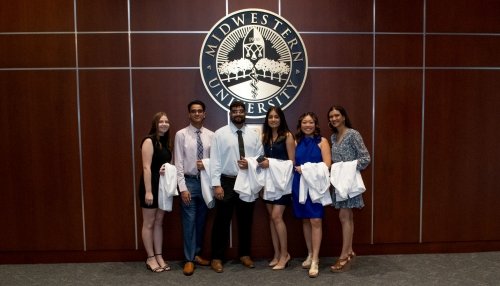 Students in line in front of Midwestern University seal.