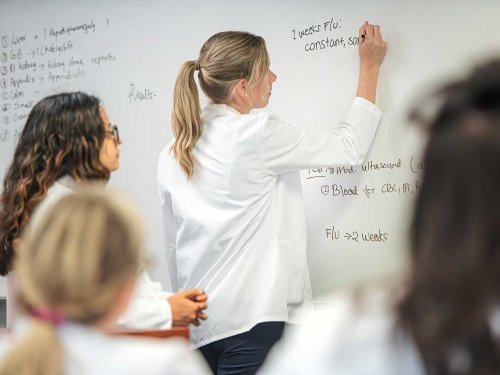 Nurse writing on whiteboard discussing health with other nurses