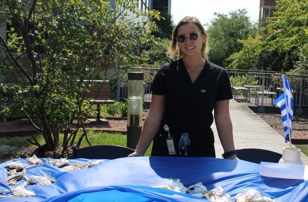 Student stands by the MWU Greek Club table with information and cultural artifacts.