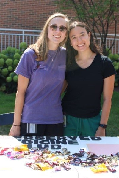 Students stand before a table with information about the Underserved Medicine Club and treats.